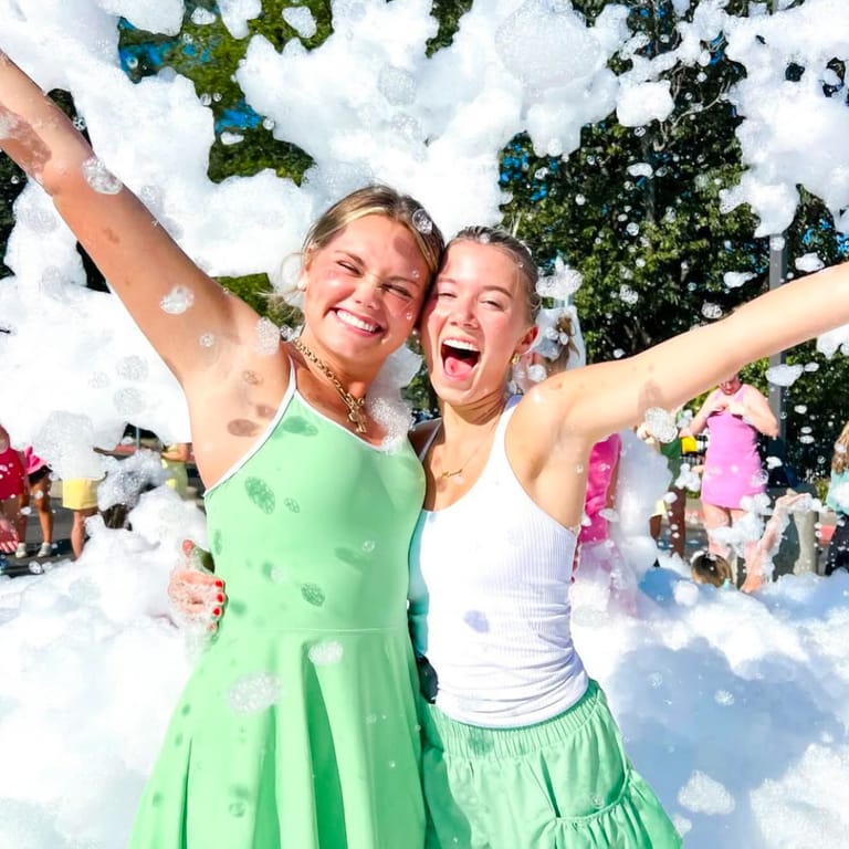 Two teenagers throwing their arms up in front of a wall of foam, both mid-laugh