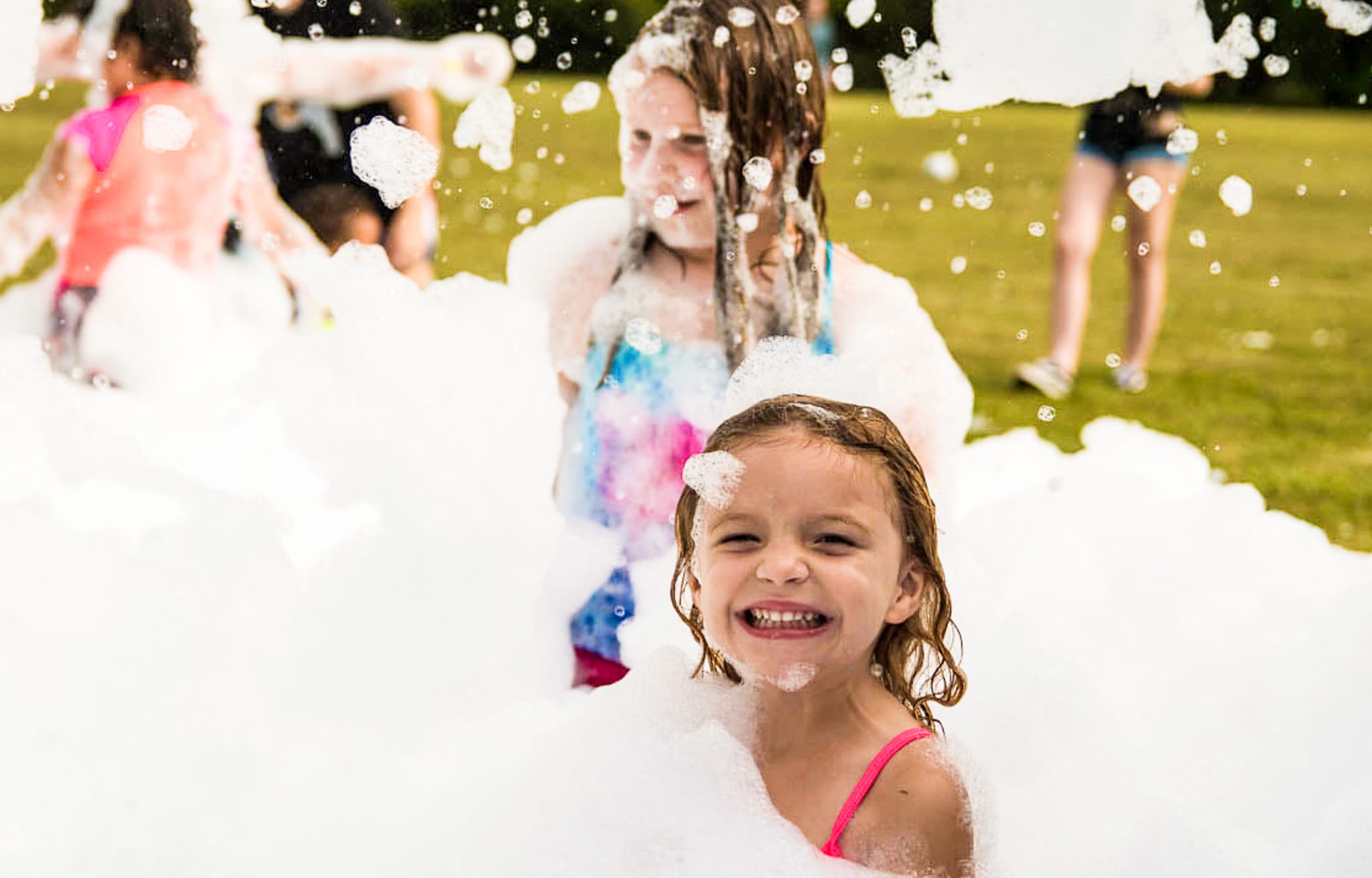 A laughing girl in a sea of foam with more kids playing behind her