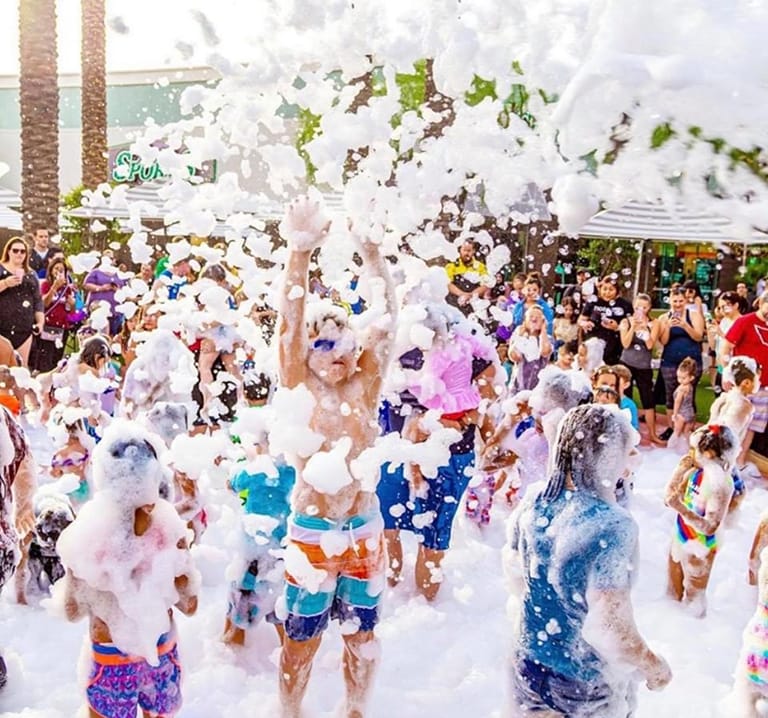 A crowd of kids playing in knee-deep foam while parents watch from the edge