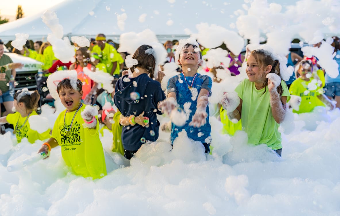A crowd of kids waist-deep in foam under a party tent, foam flying overhead